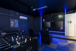 Welcome to a lively entertainment room perfect for fun and relaxation, complete with a foosball table, cozy seating, and dual screens for gaming or movies. The atmospheric blue lighting sets an engaging mood for your stay.