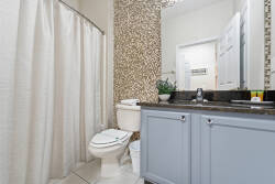 This bathroom blends functionality and style, showcasing a sleek granite countertop and a textured accent wall for warmth. Soft shower curtains enhance the airy atmosphere, creating a refreshing space to start your day.