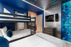 Welcome to this vibrant room with deep blue walls and geometric accents that energize your stay. Stylish bunk beds and plush bedding promise relaxation and fun, while the sleek storage unit adds practicality to your experience.