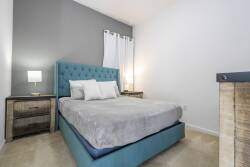 This cozy bedroom features a striking teal upholstered bed that invites relaxation, with soft gray walls and warm lighting from stylish nightstands, all creating a tranquil atmosphere perfect for restful nights.