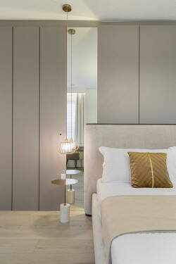 This cozy bedroom features soft beige tones and a plush bed adorned with a decorative pillow, creating a soothing atmosphere. A stylish pendant light and sleek cabinetry enhance the modern decor while offering functional elegance.