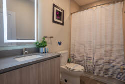 This bright bathroom boasts a sleek gray countertop and light wood cabinetry for a fresh feel. An illuminated mirror and tasteful artwork enhance the atmosphere, making your daily routines enjoyable and sophisticated.