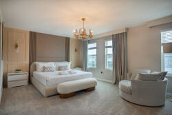 Enjoy a peaceful stay in this beautifully decorated bedroom, featuring a plush king-size bed and a cozy armchair. Soft beige tones and natural light from large windows create a serene atmosphere ideal for relaxation.