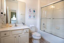 This bright and airy bathroom boasts a spacious glass-enclosed shower and a sleek vanity with plenty of storage. Charming artwork decorates the walls, and natural light floods in, creating a refreshing and inviting atmosphere.