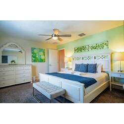 Experience a bright and airy bedroom with a plush white bed and elegant blue accents against soothing mint-green walls. Enjoy the soft glow from stylish lamps and the spacious feel created by the tasteful decor.
