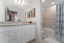 Experience this elegant bathroom with a sleek granite countertop and chic white cabinetry. Soft lighting enhances the decor, and the inviting shower area creates a warm ambiance ideal for relaxing after a long day.