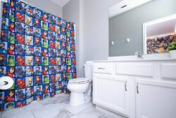 This bright bathroom features a fun superhero-themed shower curtain, sleek white cabinetry, and modern fixtures, creating a playful yet stylish space that ensures a comfortable start to your day.