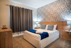 Rest in a cozy bedroom with a clean white bed, blue accent throw, wood headboard, geometric feature wall, soft lamps, gray curtains, and warm natural details, creating a comfortable space for vacation.