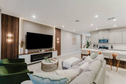 Experience comfort and style in our spacious living area, featuring a cozy sectional sofa and vibrant green armchairs. The sleek entertainment unit and modern kitchen with bar seating make it ideal for gatherings and relaxation.