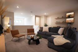 This bright and airy living room invites you to relax on a plush dark gray sectional. Natural light pours in, illuminating the stylish floating shelves and cozy accents, making it the perfect spot to unwind.