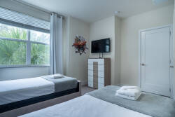 This cozy bedroom is bright and airy, featuring two comfortable beds with soft linens and large windows that let in natural light, creating a welcoming atmosphere. A stylish dresser and tasteful decor enhance your stay.