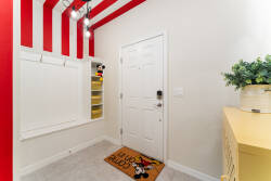 Step into a cheerful entryway featuring playful red-striped walls that create an energetic welcome. The bright space is complemented by modern lighting and a charming Mickey Mouse doormat, setting a fun tone for your stay.