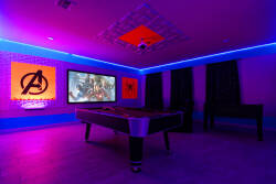 Step into this vibrant game room, where neon blue lighting creates a lively atmosphere. The sleek pool table invites friendly competition, while striking superhero art adds a playful touch to your downtime.