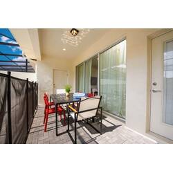 Enjoy outdoor meals on a covered patio with a black dining table, red chairs, sliding glass doors, pool view, and paved flooring, creating a relaxed space for vacation moments.