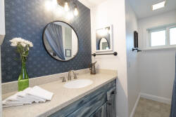 Experience a stylish bathroom with a chic blue accent wall and a sleek stone countertop, harmonizing with modern fixtures. Bask in the natural light from the skylight while fresh towels are ready for your comfort.