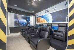 Step into this immersive home theater, featuring plush black recliners that invite relaxation while you enjoy your favorite films. The cosmic wall murals create a unique atmosphere, making every movie night an adventure in style.
