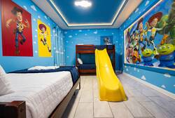 Sleep in a bright Toy Story themed bedroom with blue cloud walls, character posters, cozy beds, a yellow slide, and soft ceiling lighting, creating a fun space for kids.
