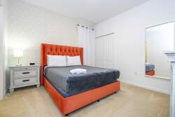 This vibrant bedroom showcases a striking orange tufted headboard that adds color to the light walls. Cozy gray bedding invites relaxation, while the sleek nightstand and large mirror enhance the room's modern vibe.