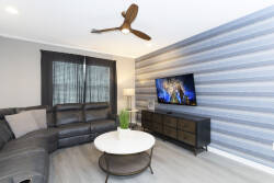 Unwind in the stylish living area featuring a cozy gray sectional perfect for gatherings. The modern overhead fan and soft blue striped wall create a serene vibe, while the round coffee table adds a contemporary touch.