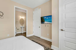 Rest in a cozy bedroom with a wall-mounted TV, warm neutral tones, wood flooring, and direct access to a private bathroom, creating a comfortable space for your stay.