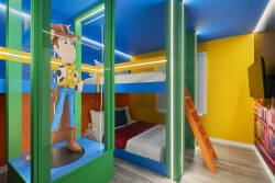 Bright colors and playful decor define this unique kids' bedroom, featuring a vibrant blue ceiling and a fun bunk bed setup. A cheerful Woody figure adds a whimsical touch, making this space perfect for imaginative adventures.