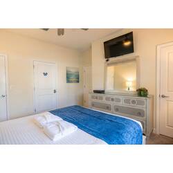 This cozy bedroom boasts a comfortable bed adorned with a plush blue throw blanket, creating a calming atmosphere. A stylish dresser matches the light walls, while a large mirror and wall-mounted TV provide practicality and charm.