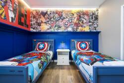 This vibrant kids' room features bright blue walls and twin beds with colorful superhero bedding, creating an exciting atmosphere for imaginative play and restful nights, enhanced by a bold mural and playful decor.