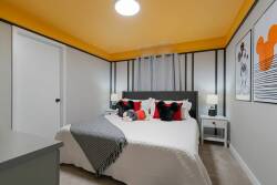 This bright bedroom boasts a striking yellow ceiling that enhances the chic black and white decor. With a plush bed adorned with colorful pillows and stylish art pieces, it creates a welcoming space perfect for relaxation.