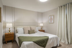 Relax in a cozy neutral bedroom with a comfortable bed, soft curtains, warm bedside lamps, wood nightstands, and simple decor, creating a peaceful space for vacation rest.