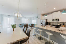 Enjoy a bright and airy kitchen featuring a spacious island with sleek bar stools for casual dining. Light blue accents and large windows fill the space with natural light, creating an inviting atmosphere for your stay.