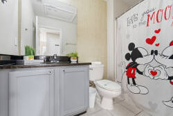 Enjoy a playful bathroom with a cheerful Mickey and Minnie shower curtain that adds whimsy. The sleek granite countertop and light gray cabinetry create a fresh, bright atmosphere for your stay, making it a delightful retreat.