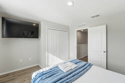 Rest in a bright bedroom with a cozy white bed, soft blue throw, gray pillows, abstract wall art, natural light, and white curtains, creating a calm space to enjoy your vacation.