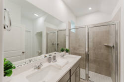 Welcome to a beautifully designed bathroom with dual sinks on a sleek quartz countertop and a spacious glass-enclosed shower. The neutral tile and bright lighting make it a refreshing retreat to unwind after your adventures.