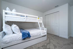 This bright and cozy bedroom features a sleek white bunk bed with plush pillows and a soft blue throw, ideal for children or guests. The neutral tones and light carpeting ensure a warm, inviting space for restful nights.