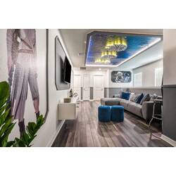 Experience a vibrant living area where modern art meets comfort, featuring a sleek gray sofa and bright blue ottomans. The unique ceiling design adds warmth, creating an inviting space ideal for relaxation or socializing.