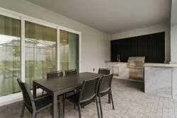 Step outside to a stylish patio featuring a sleek outdoor kitchen and a spacious dining table, ideal for gatherings. Large sliding doors bring in natural light, enhancing the modern decor and creating a warm, inviting atmosphere.