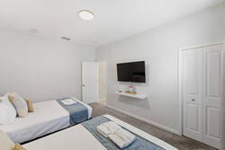 Rest in a bright bedroom with two comfortable beds, soft white bedding, blue headboards, gray curtains, bedside lamp, wall art, carpeted floor, and warm neutral decor.