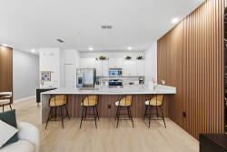 Experience this chic kitchen with sleek white cabinetry and a warm wood accent wall. The spacious island with bar seating creates an inviting atmosphere, making it the ideal spot for casual gatherings and culinary adventures.