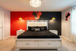 Rest in a Mickey themed bedroom with a cozy bed, bold red and black accent wall, yellow pendant lights, soft curtains, and playful character decor, creating a fun and comfortable space for vacation.