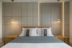 Enjoy peaceful nights in this stylish bedroom with a plush bed adorned in crisp white linens and a cozy gray throw. The warm wood nightstands enhance the modern textured wall, creating a sophisticated and inviting atmosphere.