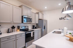 This contemporary kitchen boasts sleek gray cabinetry and a spacious white countertop ideal for meal prep or a casual breakfast. Stylish stainless steel appliances and modern pendant lighting enhance its functionality and charm.