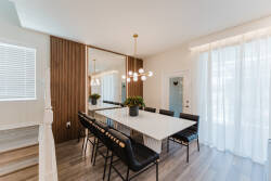 Enjoy a stylish dining area with a long marble table and elegant black chairs, ideal for gatherings. The warm wood paneling adds sophistication, and natural light from sheer curtains creates a bright, inviting atmosphere.