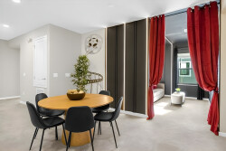 This dining area features a stylish round wooden table surrounded by sleek black chairs, setting a warm tone for meals together. Bold red curtains frame the entrance to a cozy living space, inviting relaxation and connection.
