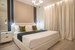 Experience a cozy bedroom with a plush bed featuring soft green accents and elegant cream curtains that let in natural light. Chic wall paneling adds sophistication, creating a delightful haven for your relaxation.