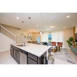 Enjoy an open kitchen and living area with a granite island, pendant lights, dark cabinets, cozy seating, dining space, soft curtains, and pool views for comfortable vacation moments.