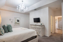 Experience a bright and cozy bedroom featuring plush turquoise pillows on a pristine white bed, an elegant chandelier casting a warm glow, and tasteful decor that invites you to relax in this tranquil space.