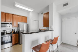 This bright kitchen boasts warm wooden cabinets and sleek stainless steel appliances. Enjoy your morning coffee at the stylish bar with textured seating, soaking in the natural light that fills the space.