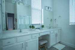 This bright and airy bathroom boasts a spacious double vanity in a clean white finish, complemented by sleek fixtures. Natural light floods the space, creating a refreshing atmosphere, while potted plants bring a serene touch.
