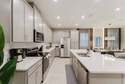 This stylish kitchen features sleek white cabinetry and a spacious island perfect for meal prep or casual dining. Modern stainless steel appliances add sophistication, and large windows fill the space with inviting natural light.