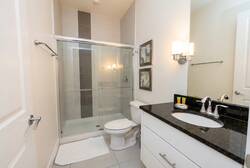 Experience a sleek bathroom with modern fixtures and a stunning contrast of dark granite and white cabinetry, offering a clean, functional space. The spacious glass shower and stylish wall accents invite refreshing moments.
